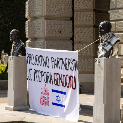 Slika s majskega protesta LDŠ pred rektoratom Univerze v Ljubljani. Na sliki je za doprsna kipa obešena zastava, na kateri piše "Projektno partnerstvo je podpora genocidu". Pod napisom sta narisana logotip Univerze v Ljubljani in izraelska zastava.