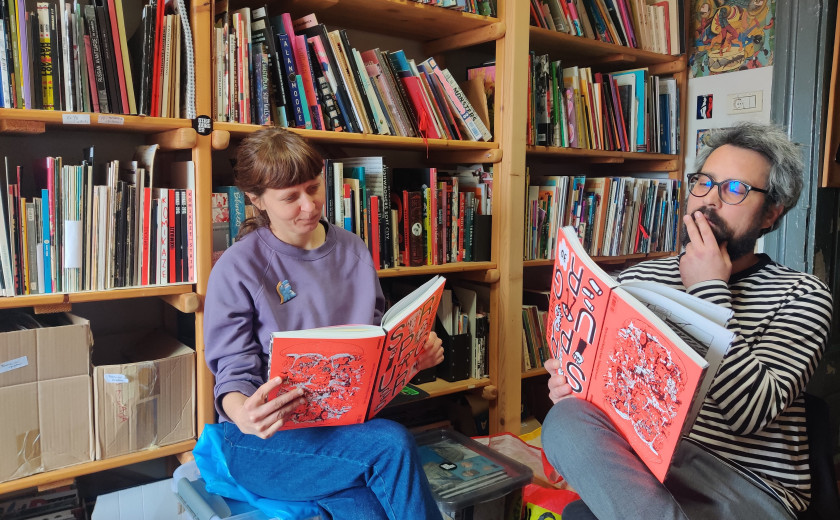 Tanja Skale in David Krančan zamišljeno prebirata izdajo Dirty Thirty v Stripburgerjevi knjižnici